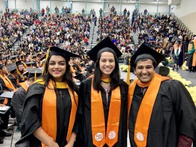 Three recent graduates pose for a picture in their cap and gown regalia.