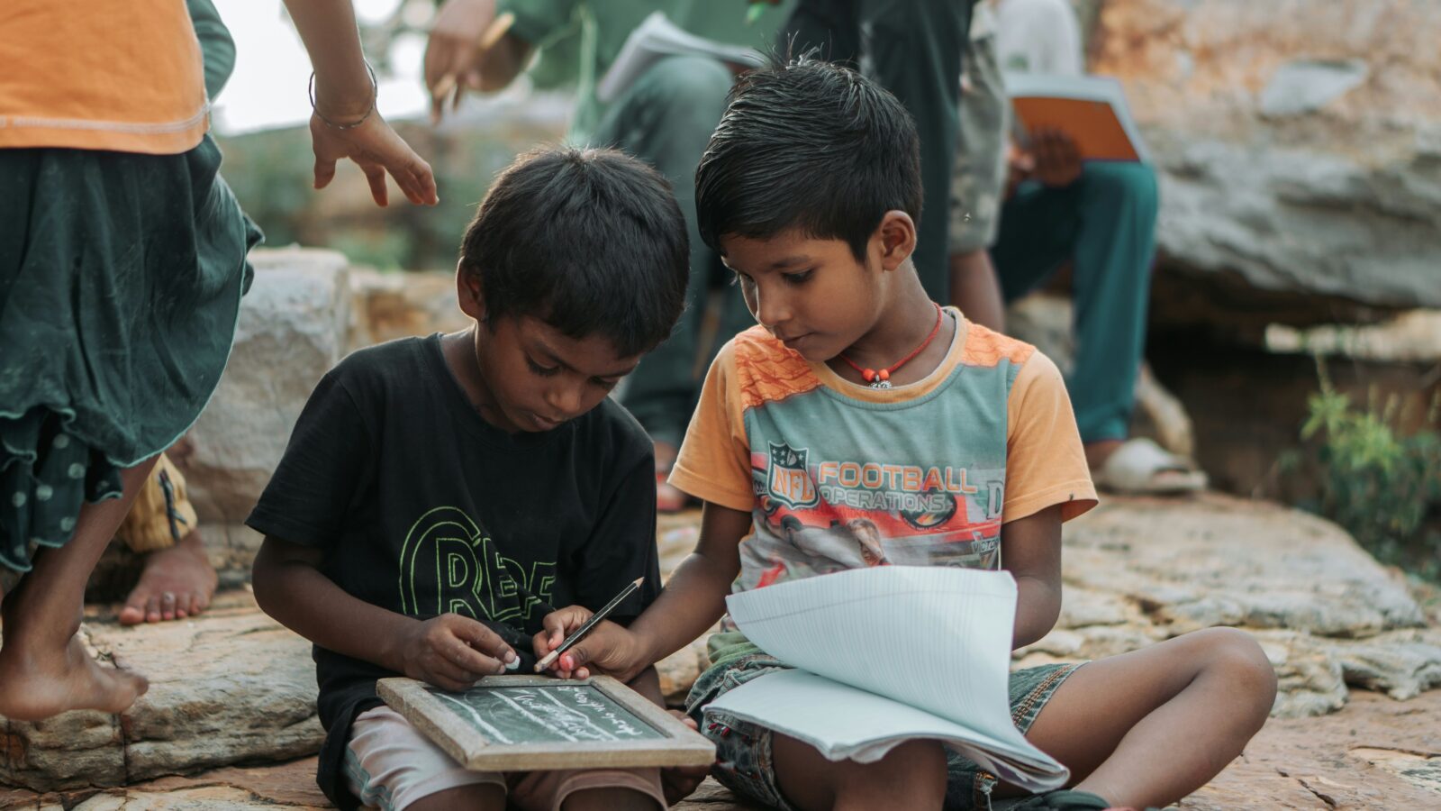 Two boys reading a book together. One helping the other.