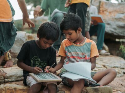 Two boys reading a book together. One helping the other.